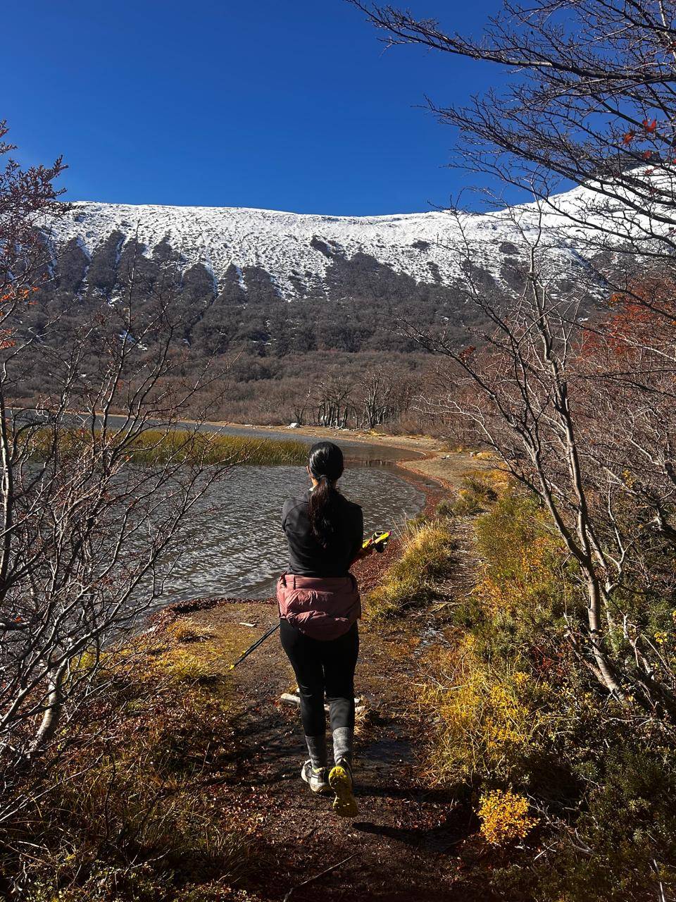 Corredora com bastões à beira de um lago, montanha nevada ao fundo